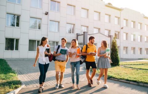 Five friendly students are walking after they passed test outside the college building and discuss the project